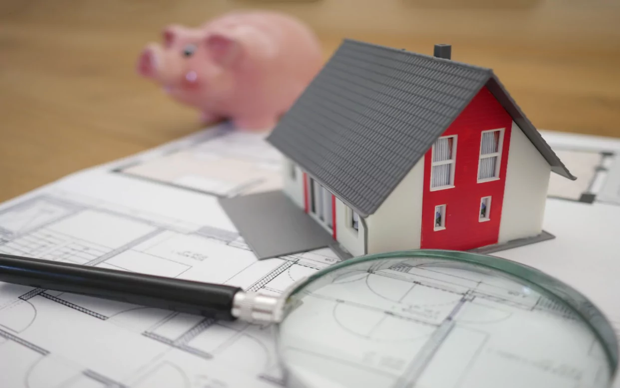 dayorama of a house, magnifying glass and piggybank on a blue print of a home